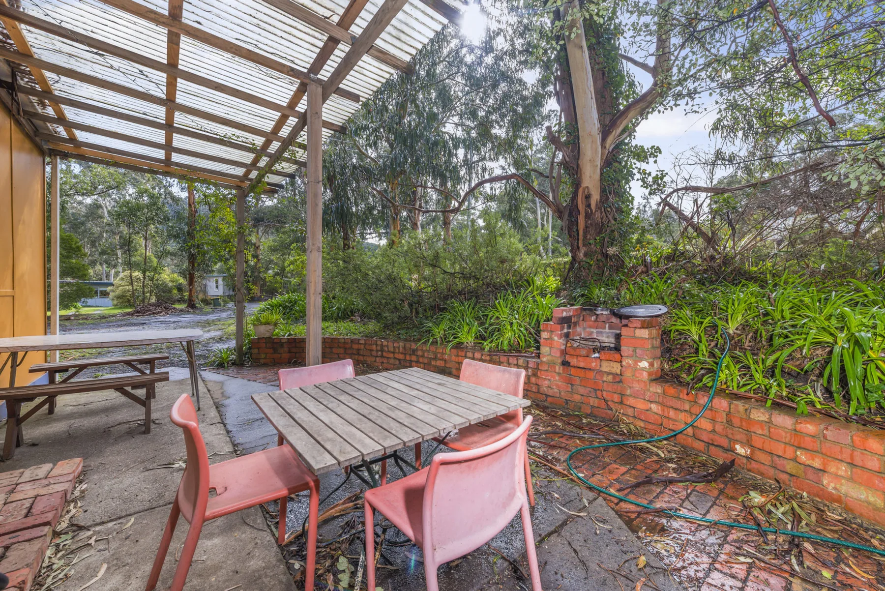 Un patio al aire libre con pérgola, mesas y árboles alrededor.
