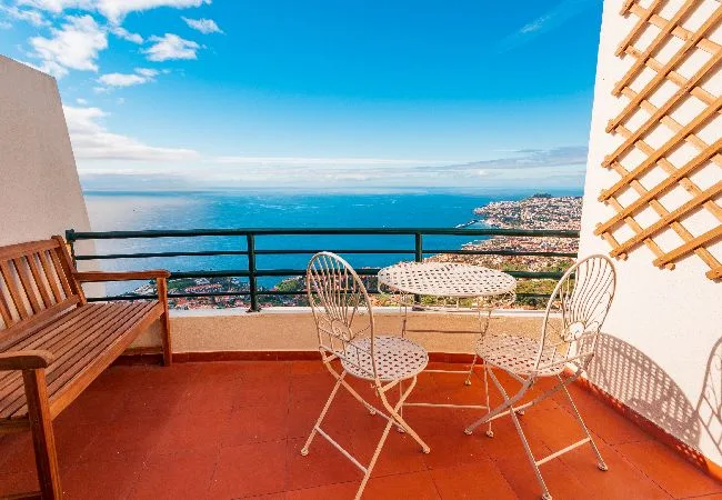 A terrace with outdoor seating overlooks the sea and a coastal town.