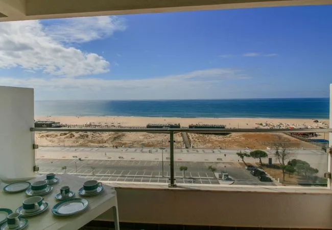 A balcony overlooks the beach and ocean, with tableware on a nearby table.
