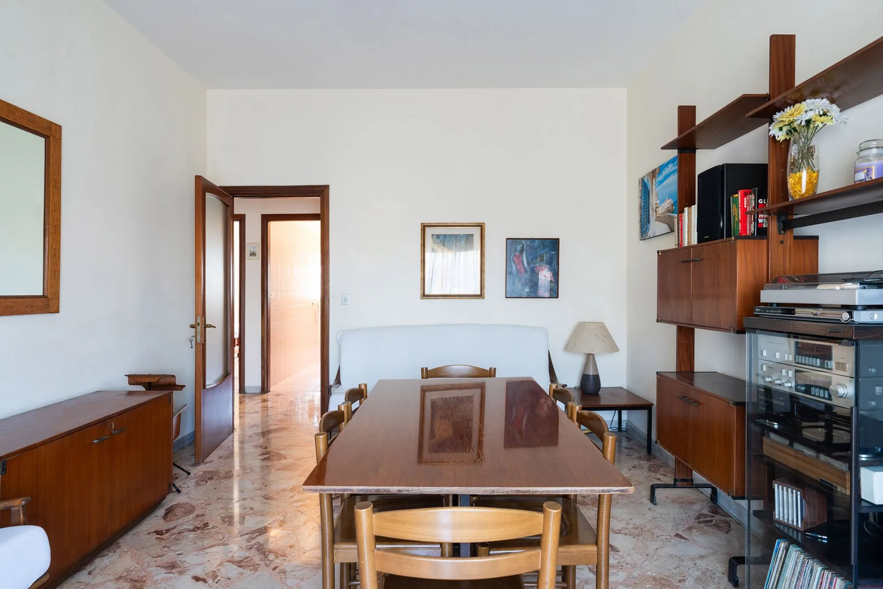 A dining room with a long wooden table and shelving along one wall.
