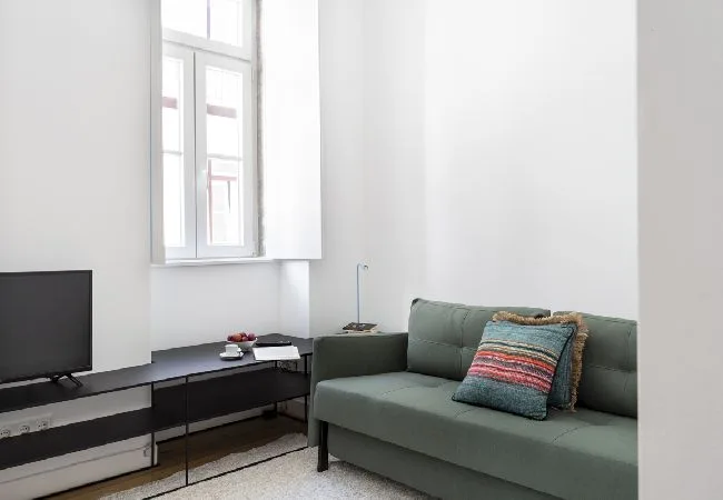 A bright living room with a green sofa, television, and large window.