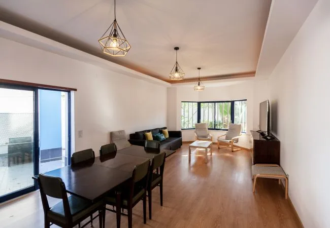 A bright living and dining area with seating, a dining table, and large windows.
