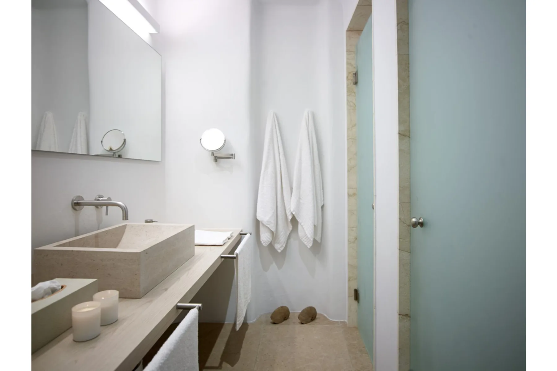 Un baño luminoso con lavabo de piedra, espejo de pared y toallas colgadas.