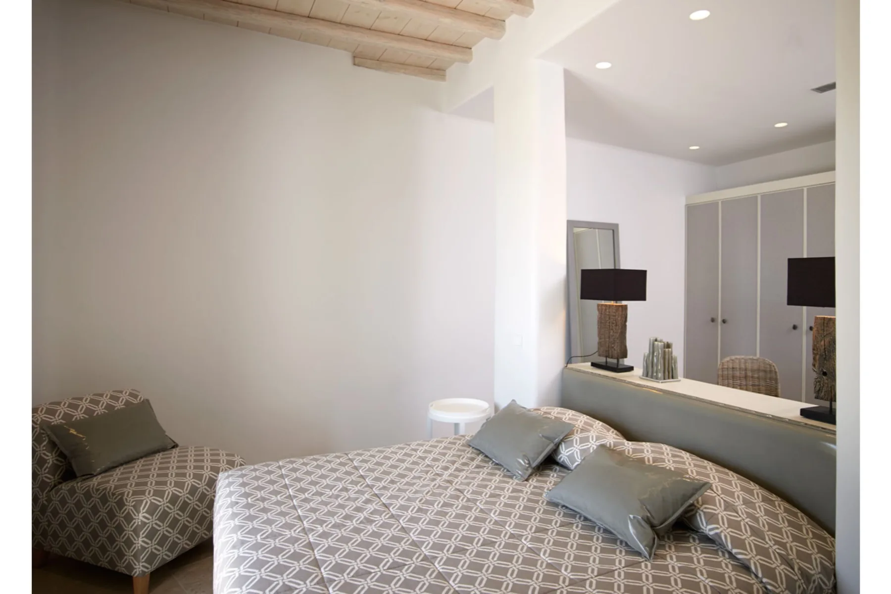 Un dormitorio con ropa de cama estampada, una cama baja y un armario con espejo.