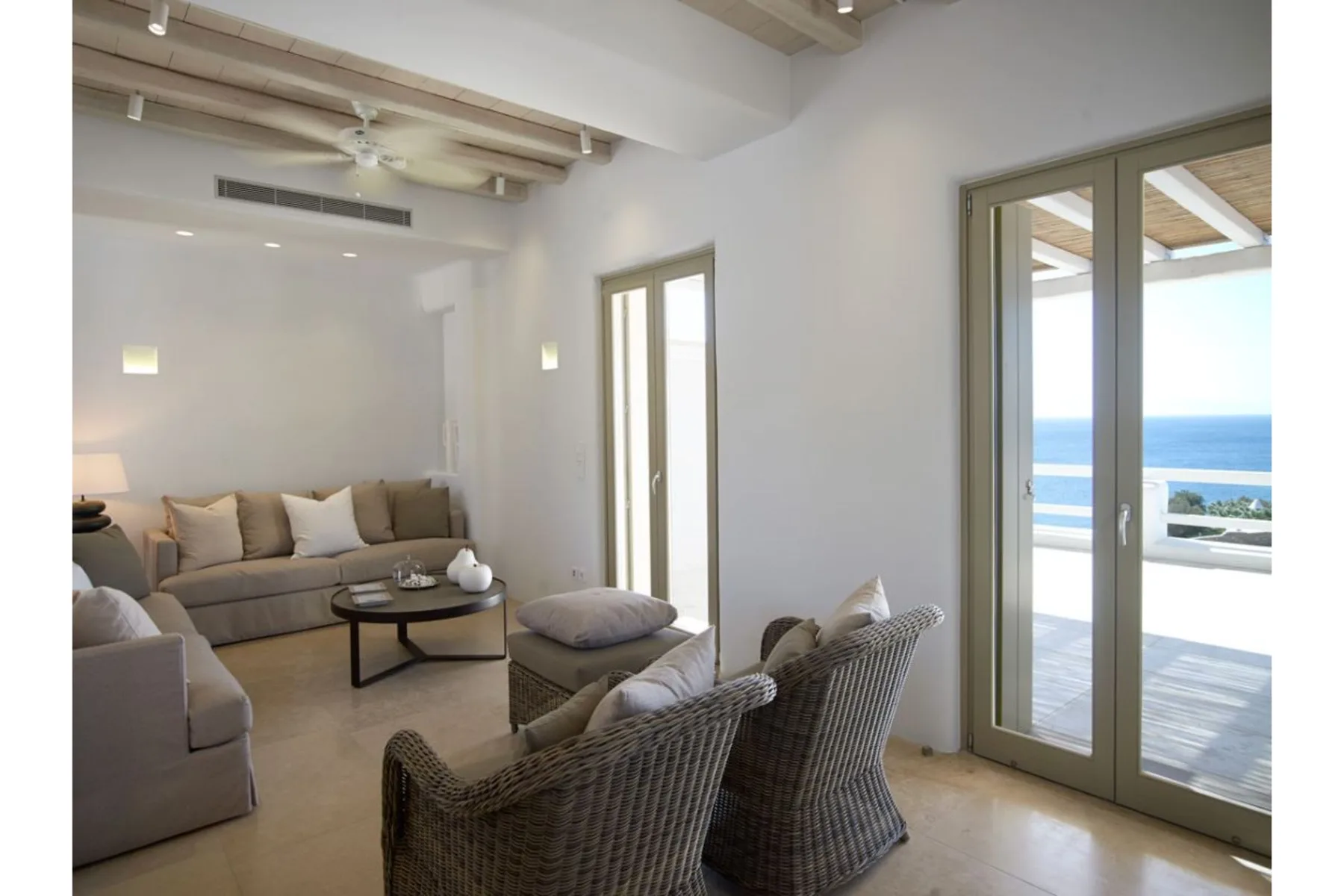 Una sala luminosa con asientos tejidos y puertas de vidrio con vista al mar.