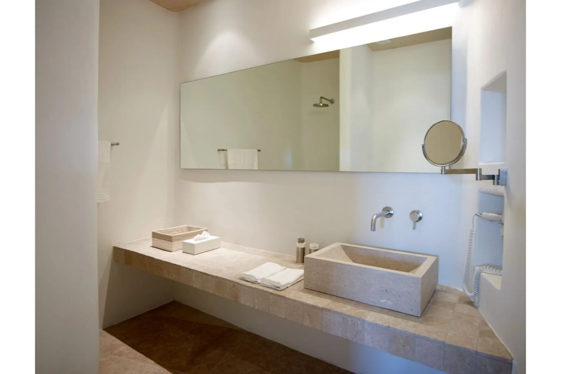 Un baño luminoso con un tocador largo, lavabo y un amplio espejo de pared.
