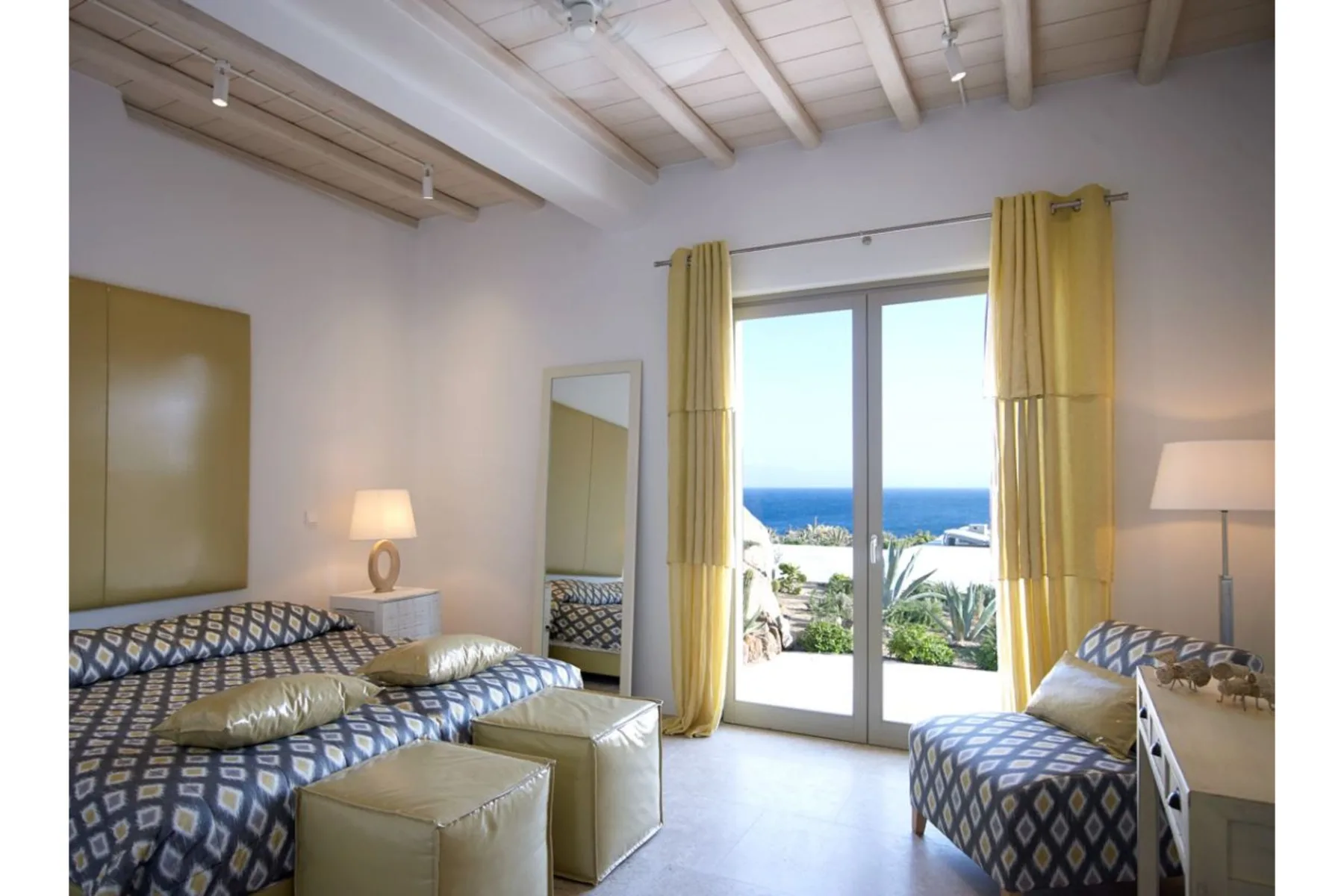 Un dormitorio luminoso con ropa de cama estampada y puertas de cristal con vistas al mar.