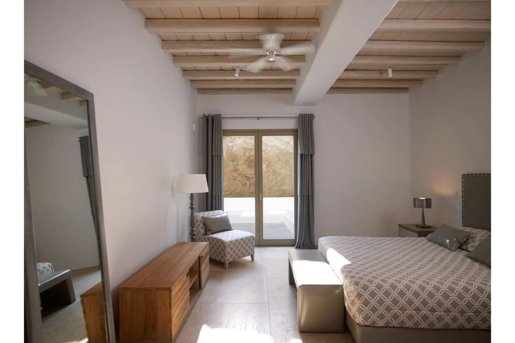 Un dormitorio luminoso con una cama grande, una cómoda de madera y puertas de vidrio.