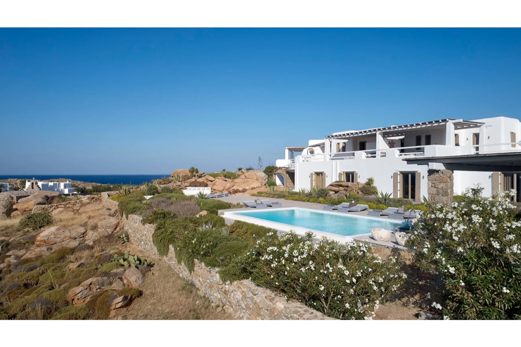 Edificios blancos junto a una piscina, un paisaje rocoso y el mar.