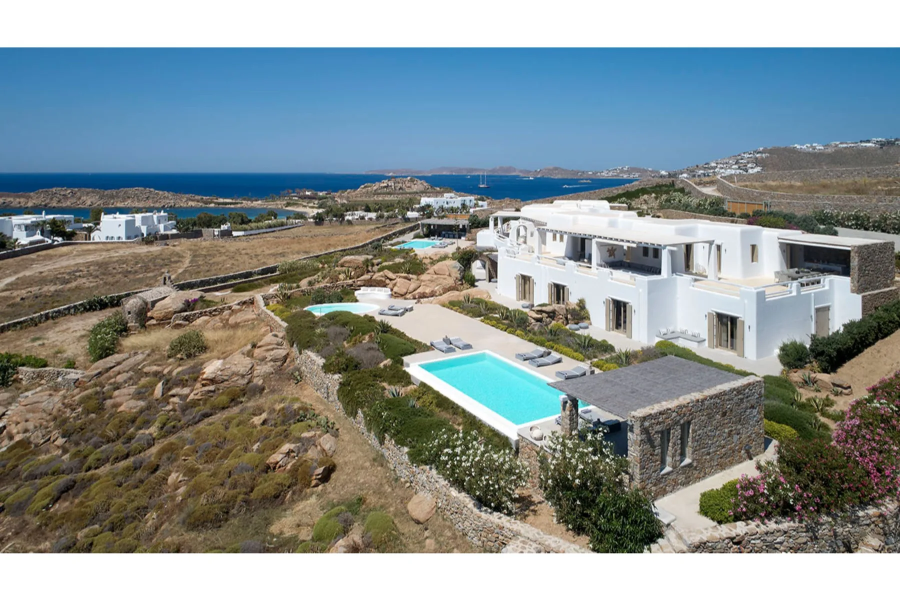 Una villa blanca domina la costa, con una piscina turquesa al frente.