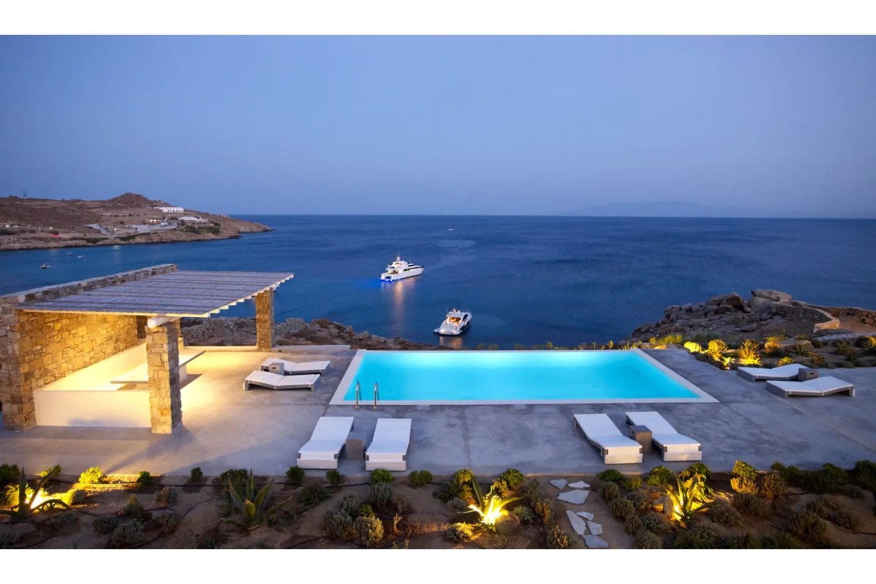 Una piscina y una terraza de piedra dan al mar al anochecer.