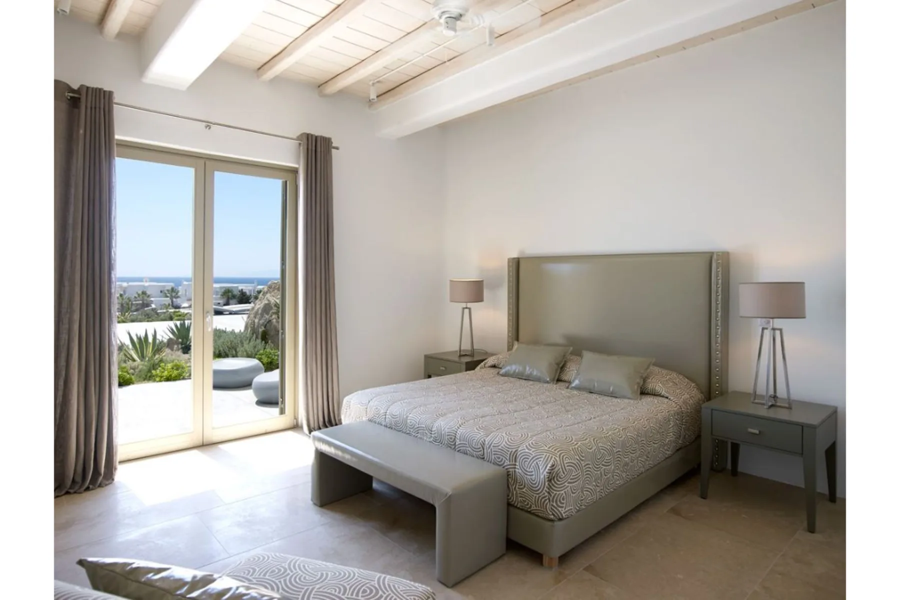 Un dormitorio luminoso con una cama grande junto a puertas de vidrio que dan a un patio.