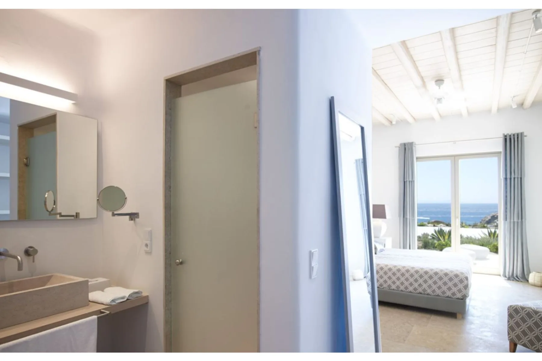 Un dormitorio luminoso se abre a un baño, con vistas al mar por la ventana.