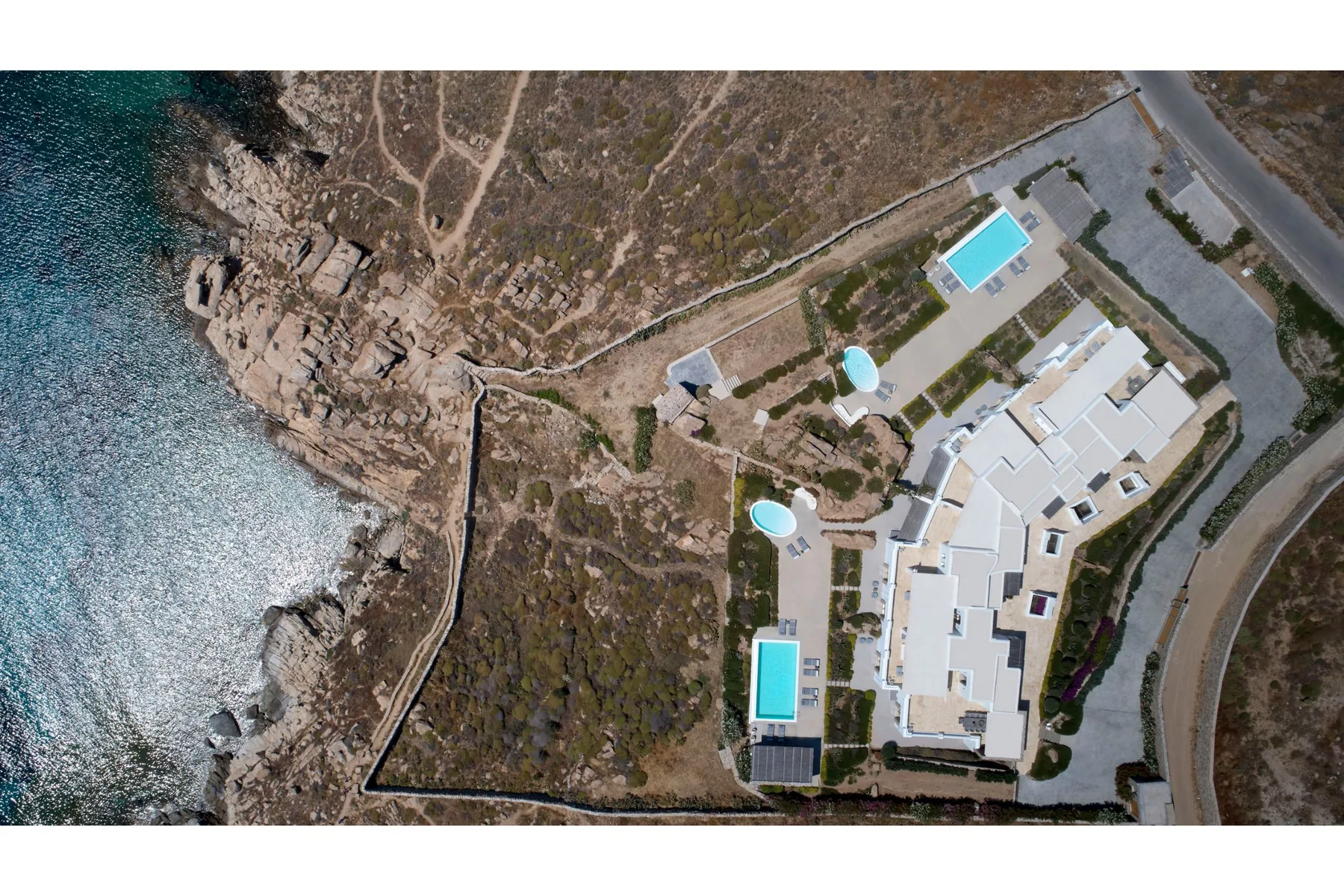 Una vista aérea muestra una propiedad costera con edificios blancos y piscinas turquesas.