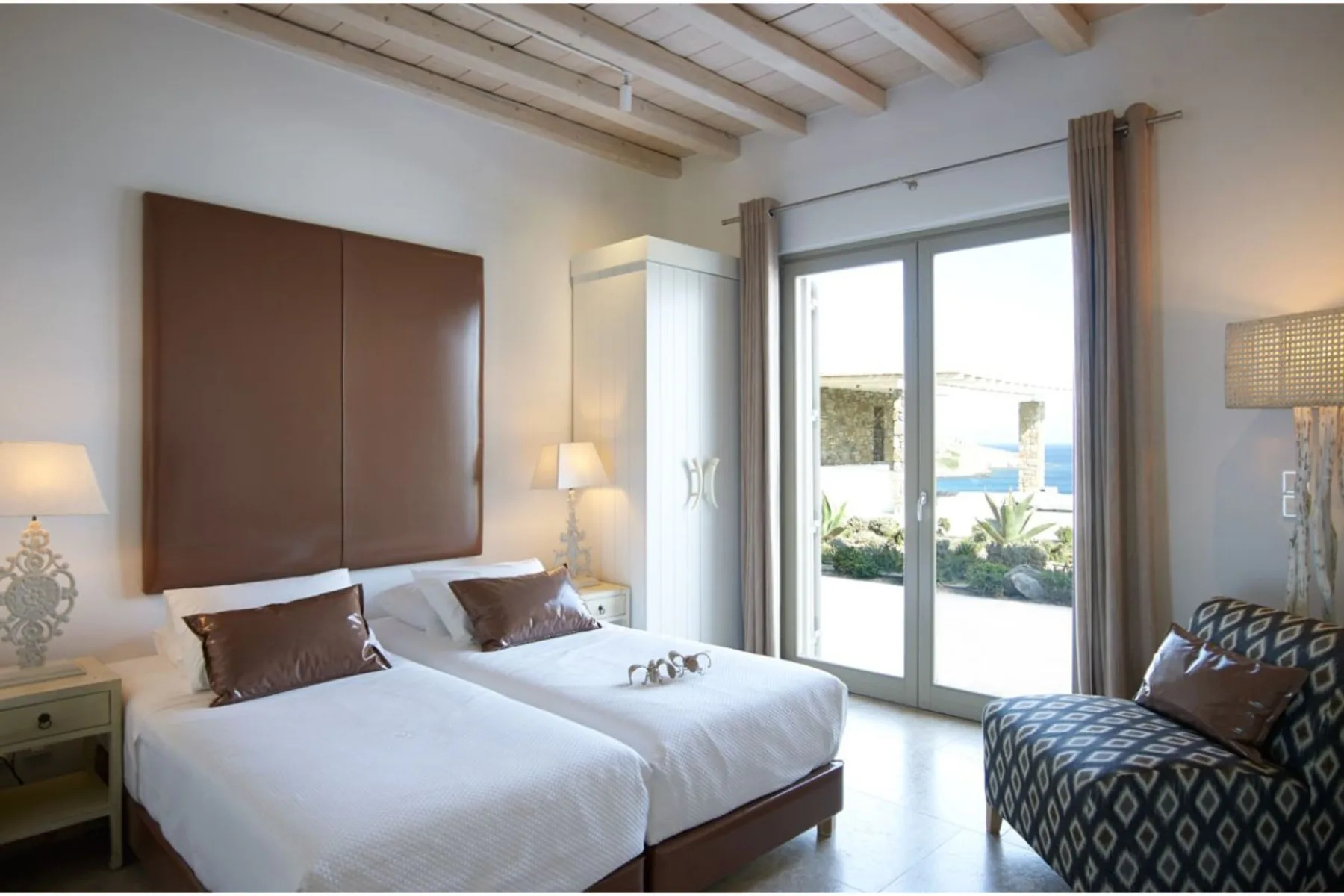 Un dormitorio luminoso con dos camas y puertas de vidrio que dan a un patio.