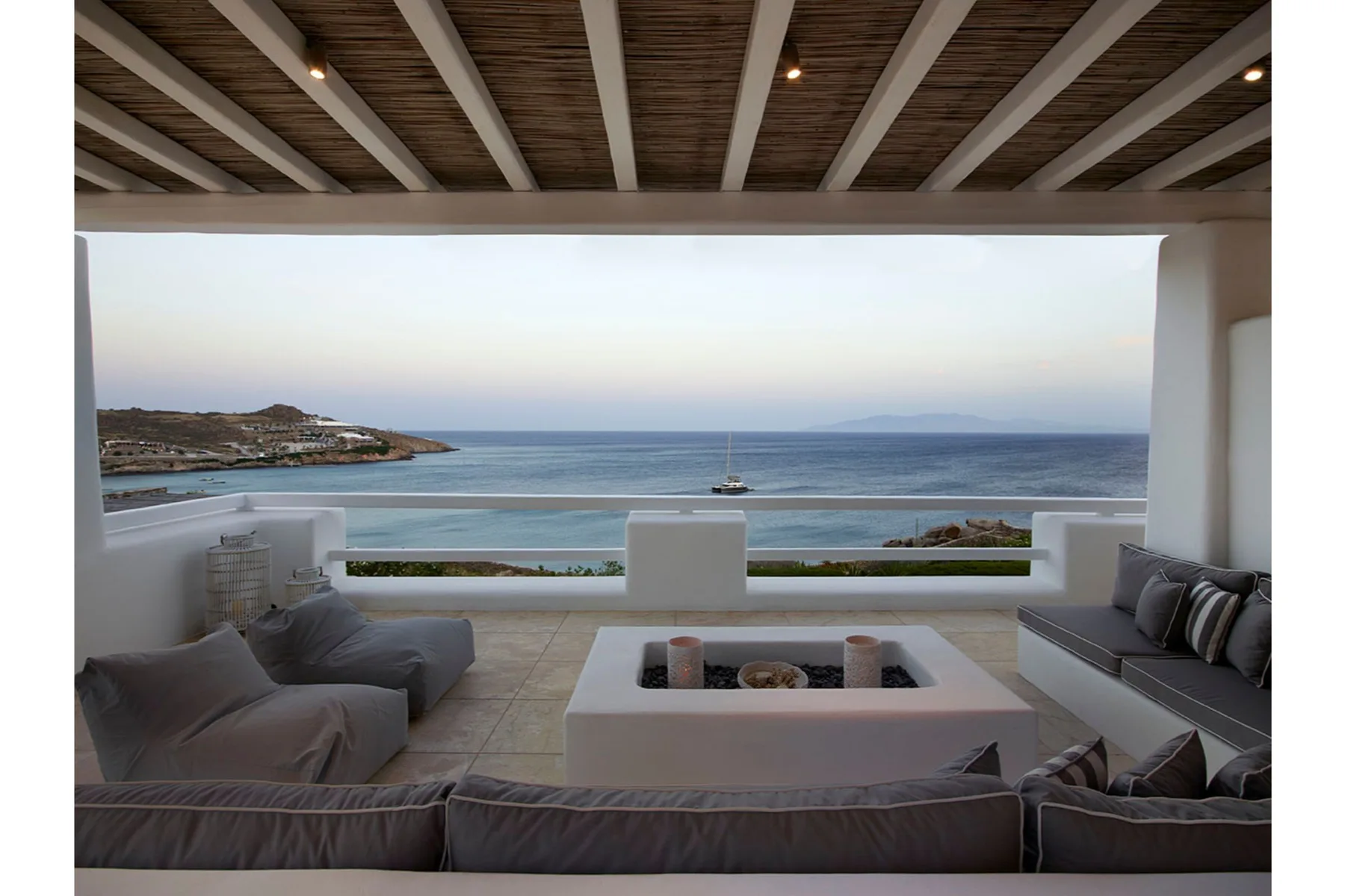 Una zona de estar exterior cubierta da al mar, con una mesa baja delante.