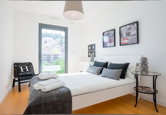 Un dormitorio luminoso con una cama bien hecha y una ventana grande.
