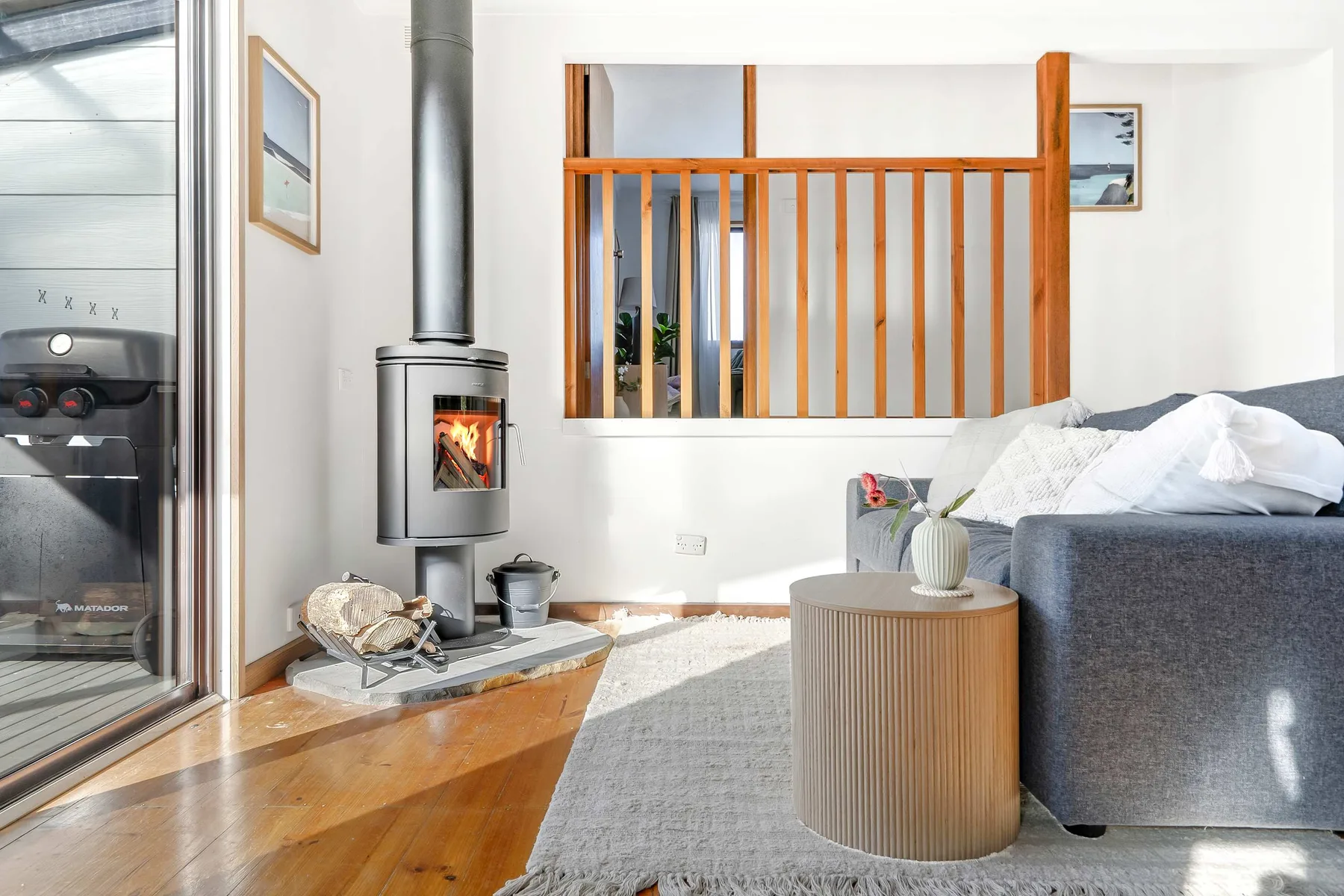 A bright living room with a gray sofa, wood stove, and round coffee table.