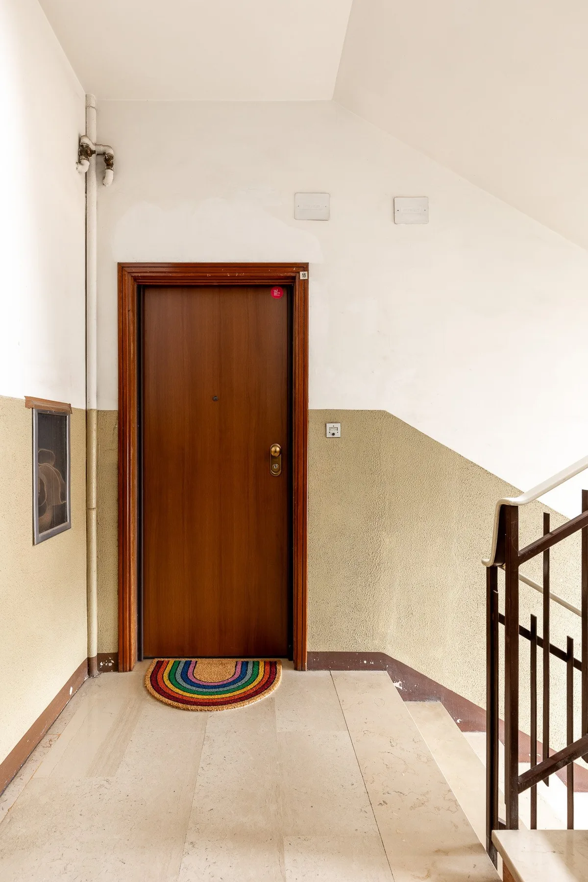Zona común: Un rellano interior con una puerta de madera y una barandilla de escalera.