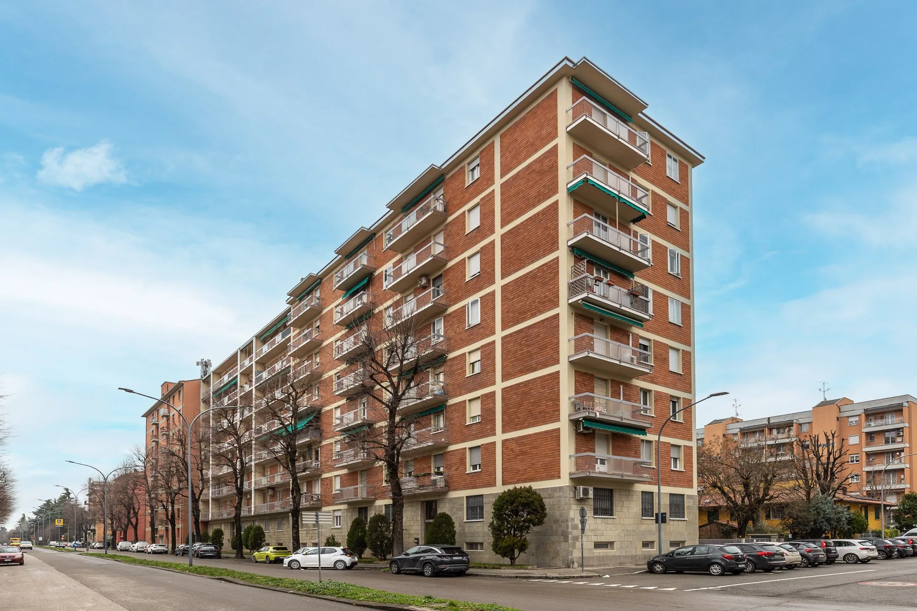 Zona común: Un edificio de apartamentos de varias plantas se alza junto a una calle con coches estacionados.