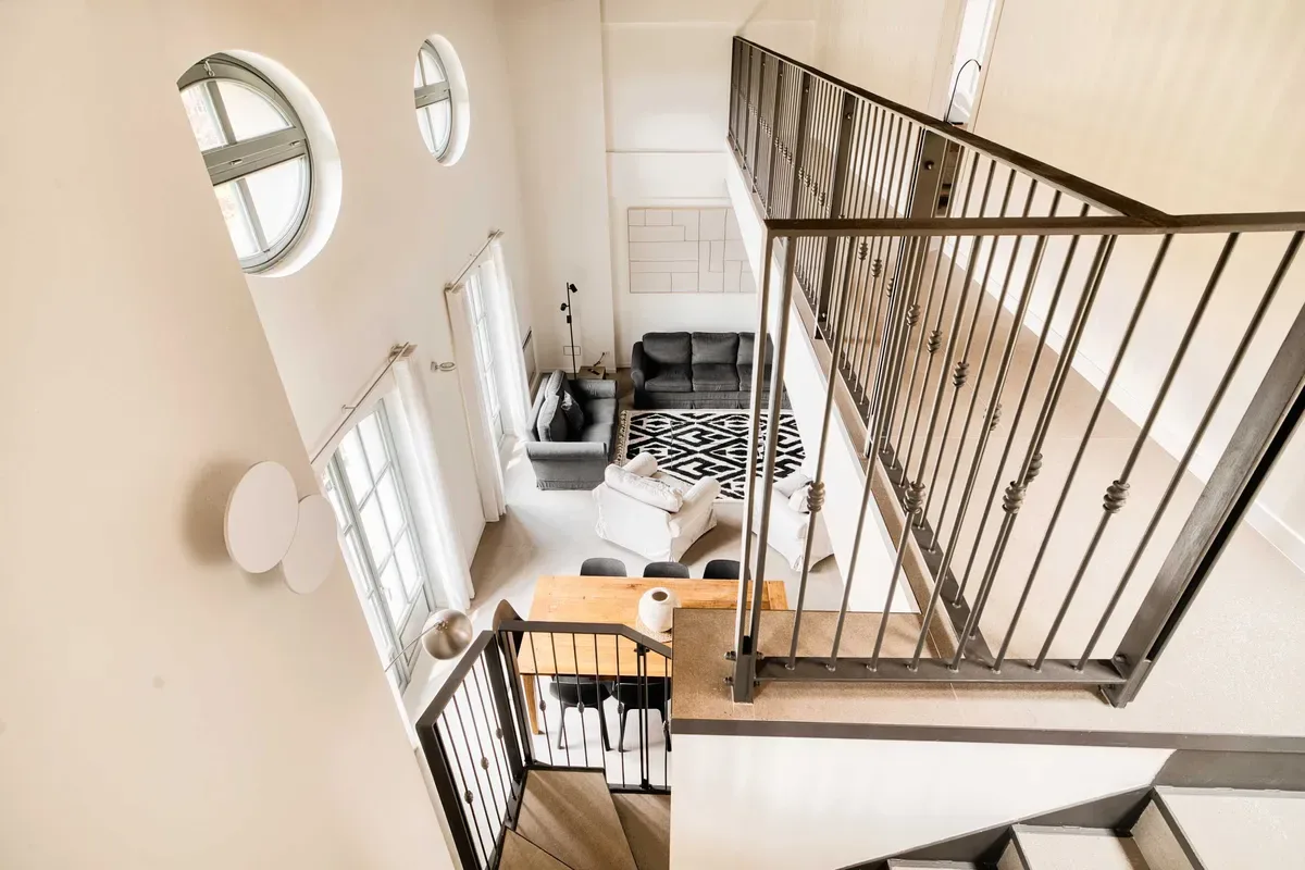 A bright living room sits beside an open staircase with dark railings.