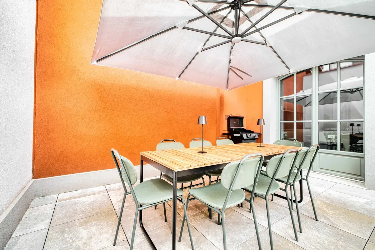 A dining area with a long table and chairs beneath a large umbrella.
