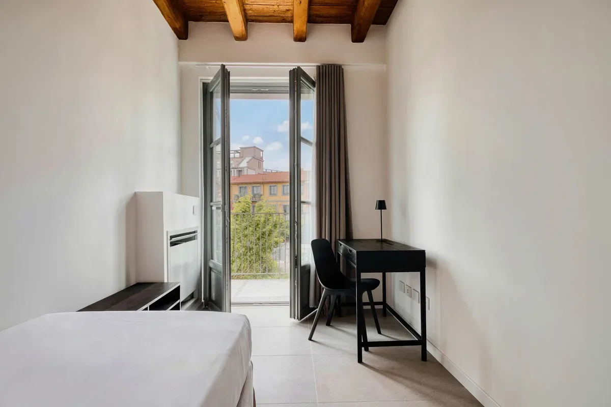 A bright bedroom with a bed, desk, and open doors to a balcony.