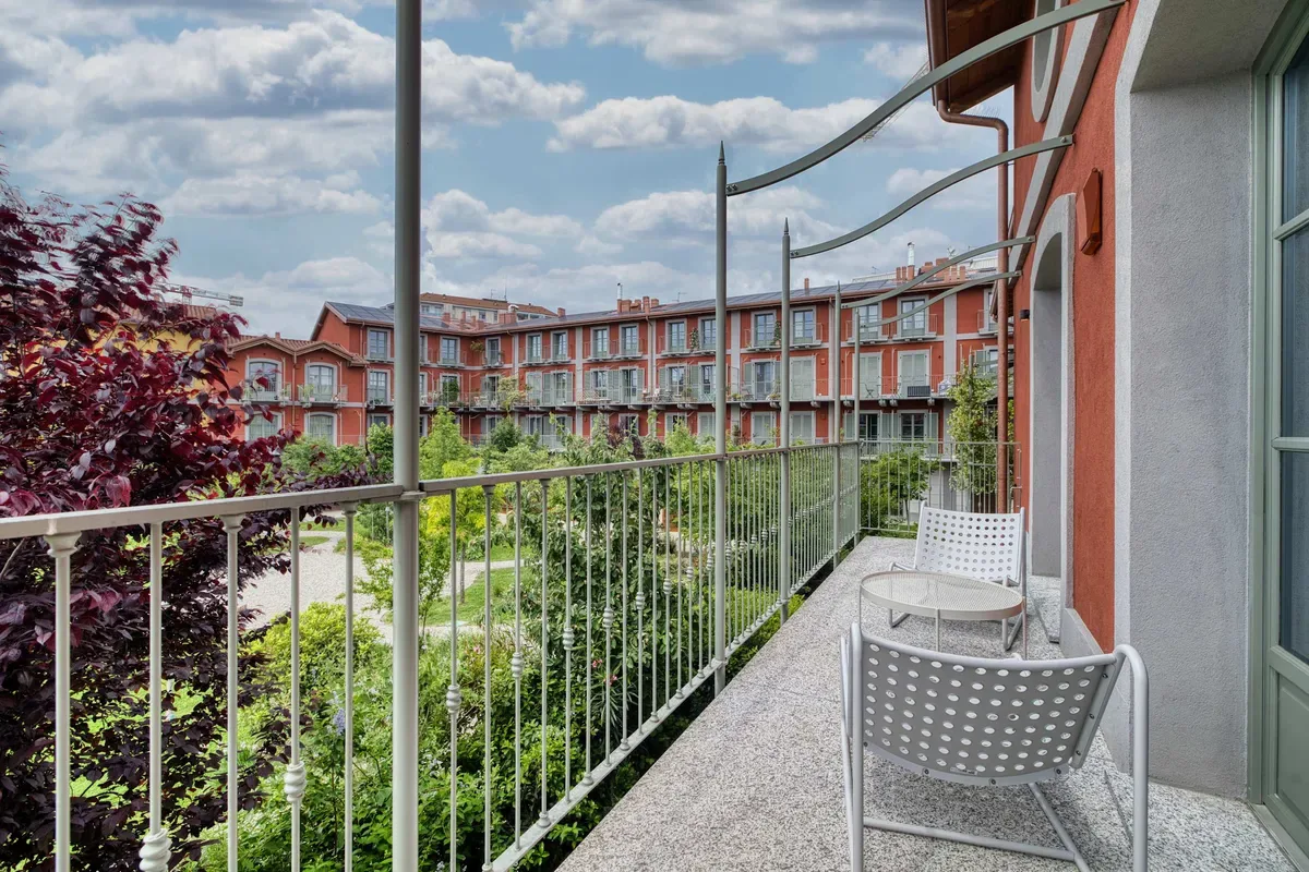 A narrow balcony overlooks a landscaped courtyard with seating and metal railings.