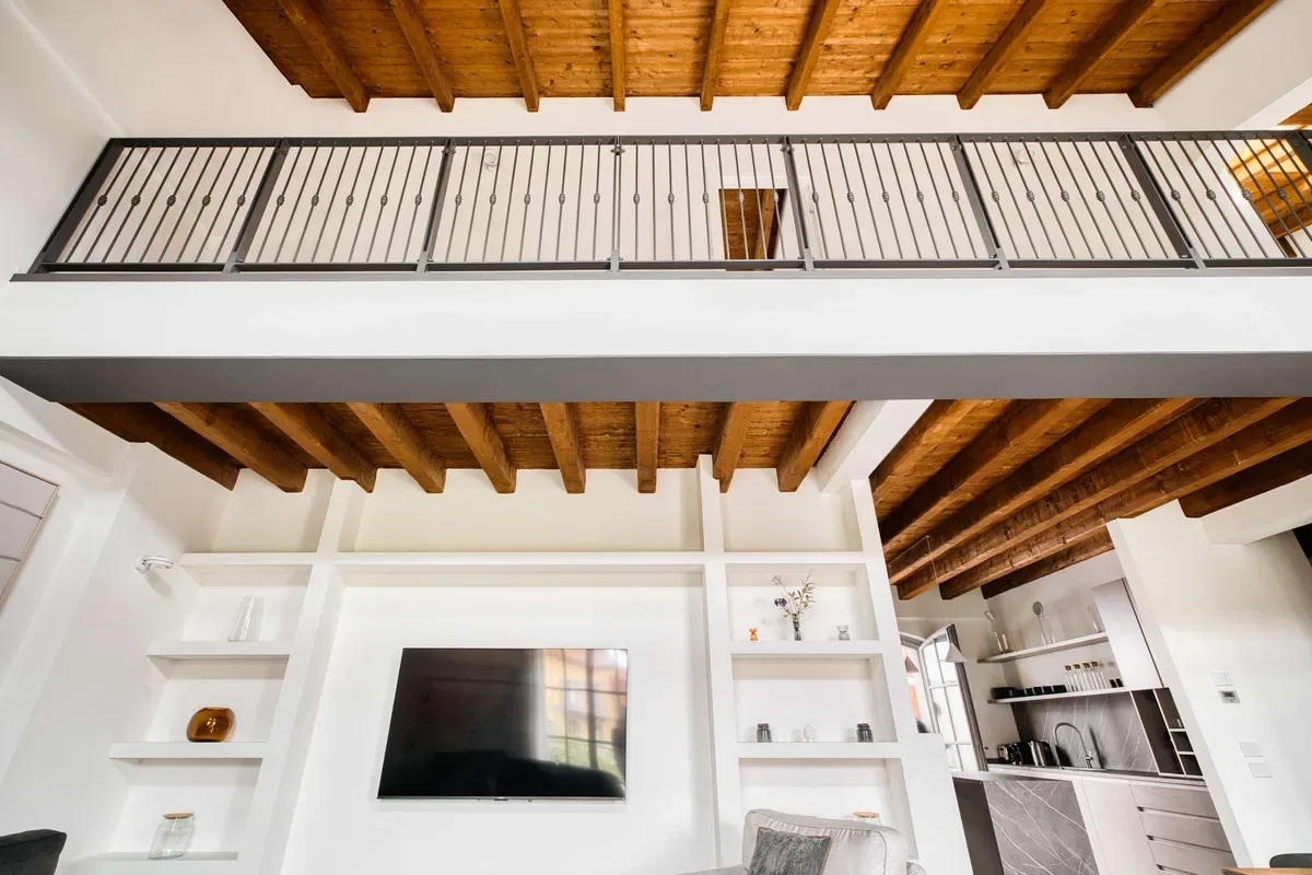 A bright living area with a wall-mounted television beneath exposed wooden ceiling beams.