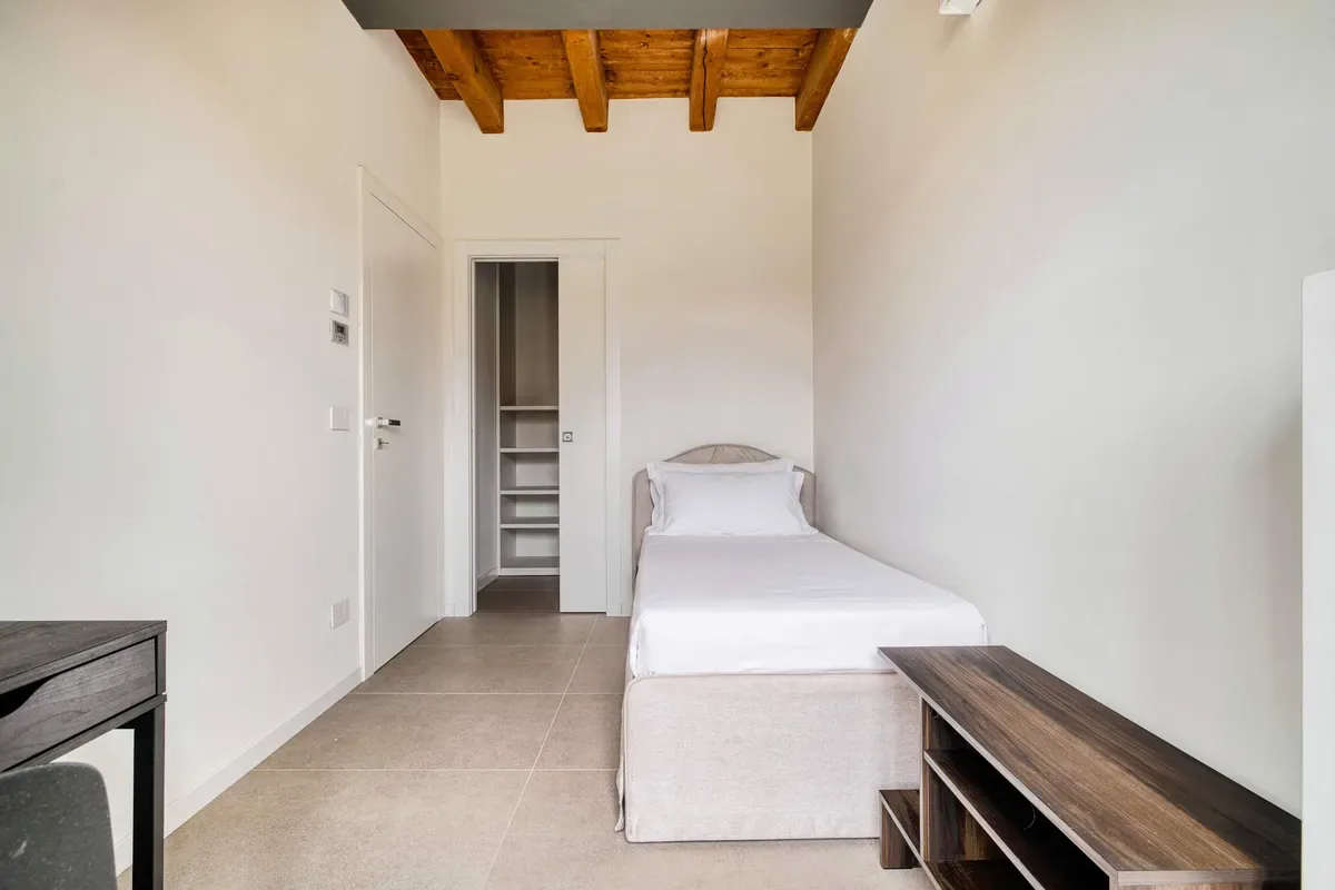 A single bed sits in a bright room with a wooden ceiling.