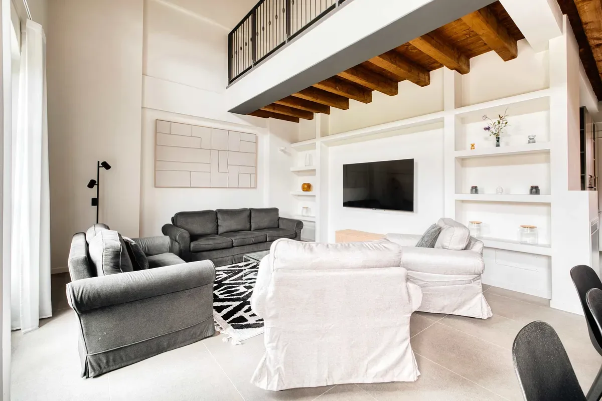 A bright living room with seating, a television, and an open wooden staircase.