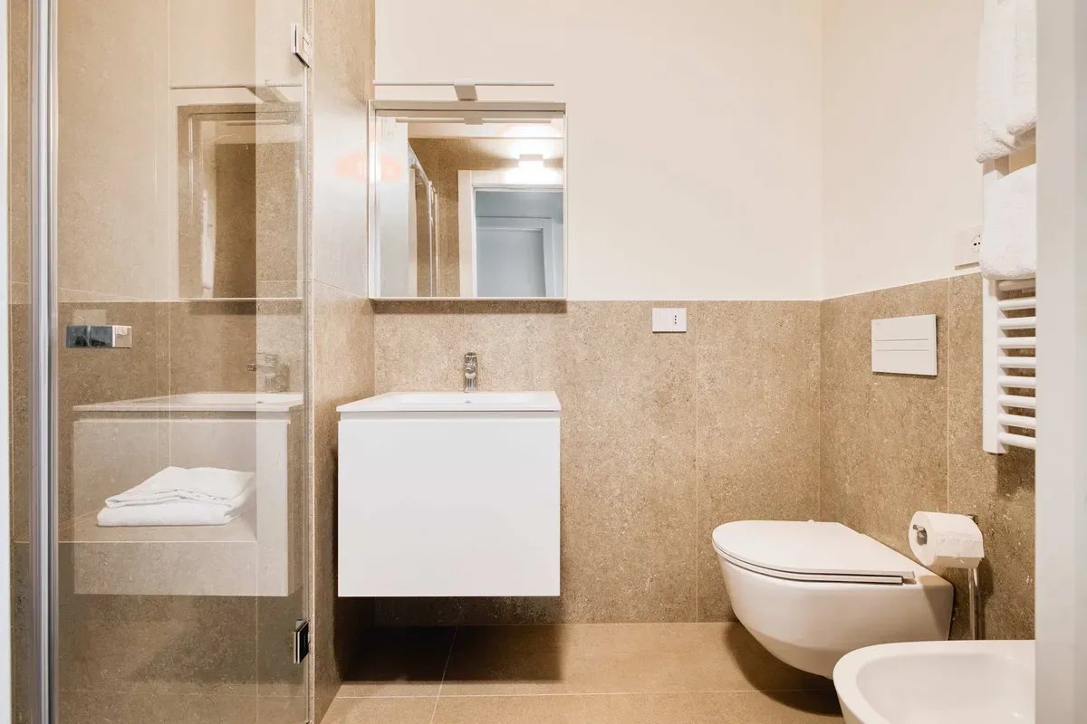 A bathroom with a wall-mounted sink, toilet, and glass shower enclosure.