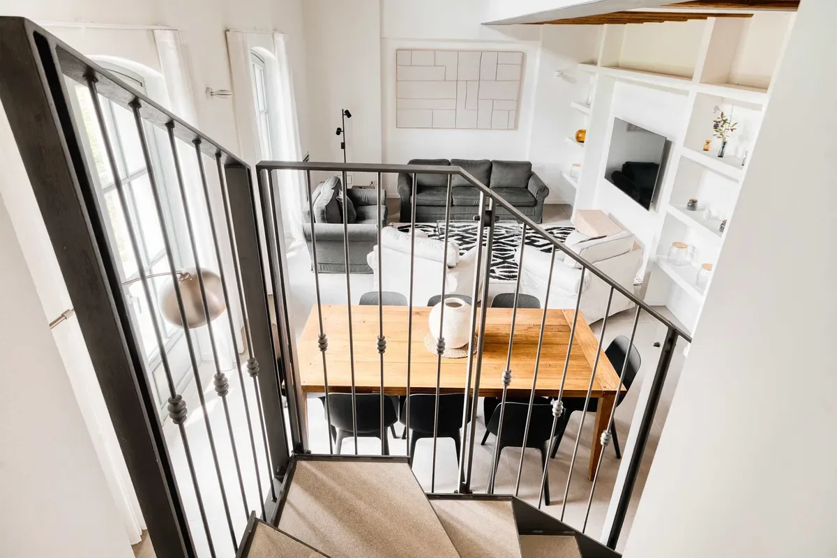 A bright living room with gray seating, a dining table, and a staircase railing.