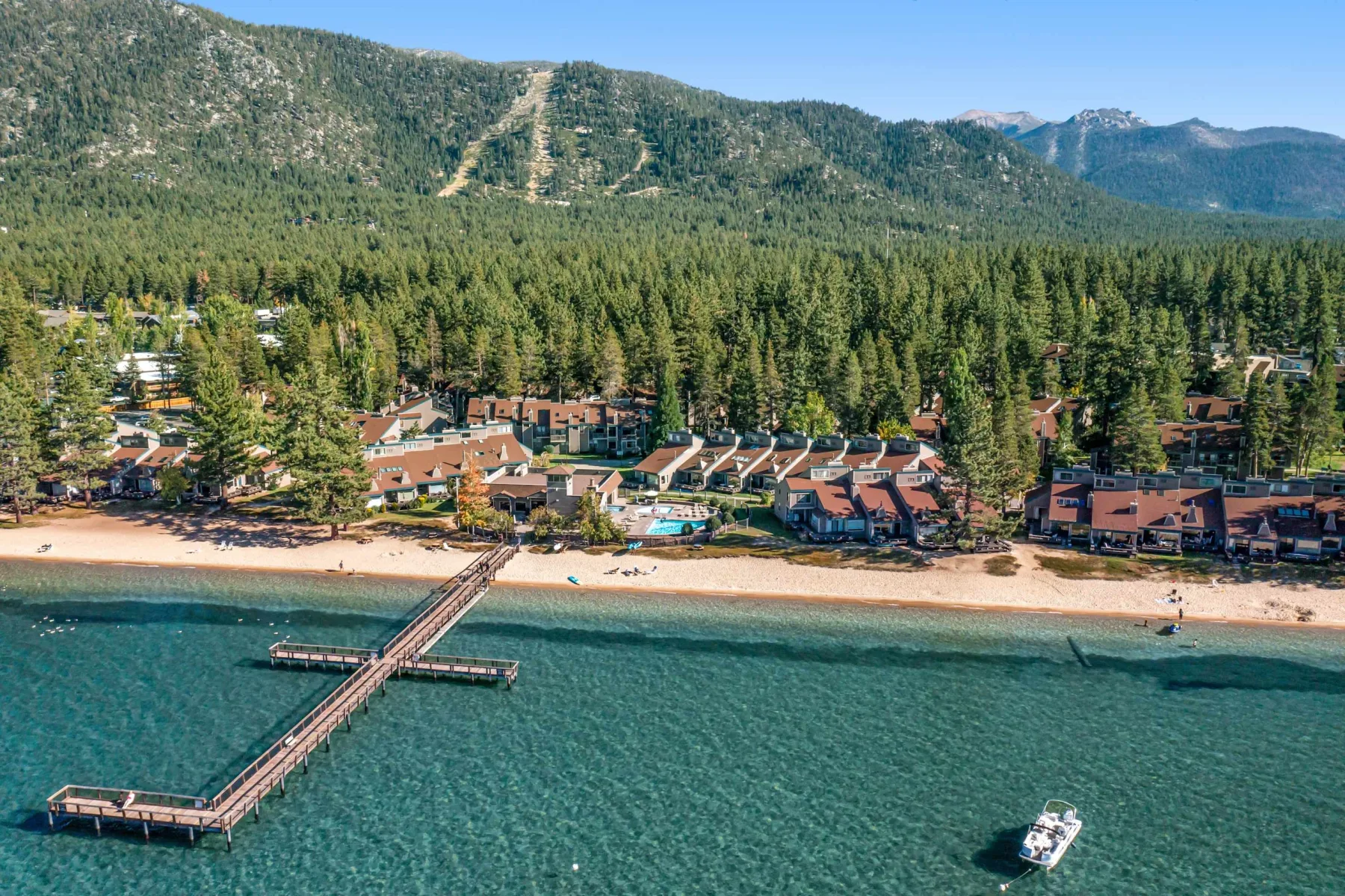 Zona común: Un complejo junto al lago con playa de arena, un muelle y montañas boscosas.