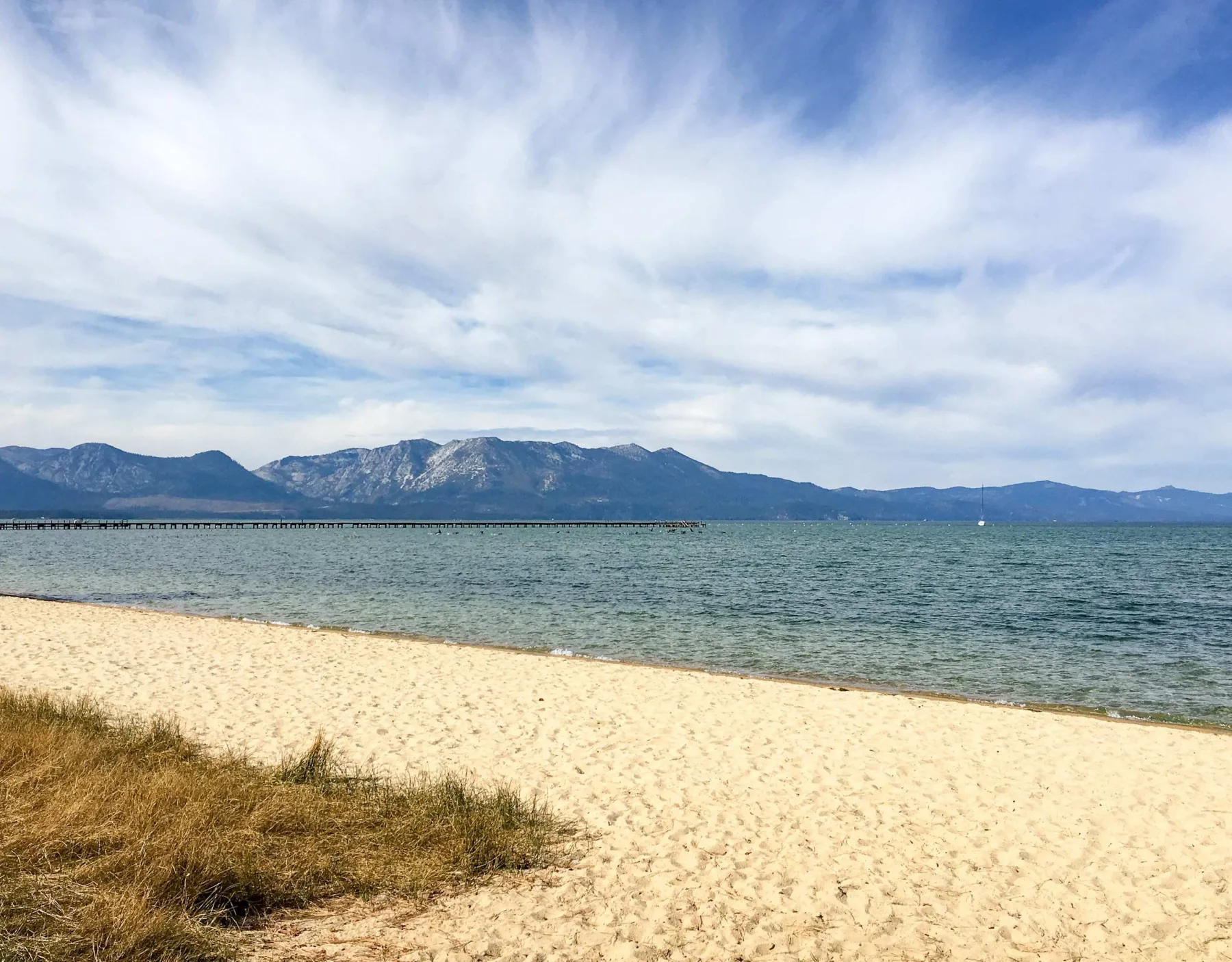 Zona común: Una playa de arena bordea aguas tranquilas, con montañas al otro lado de la bahía.