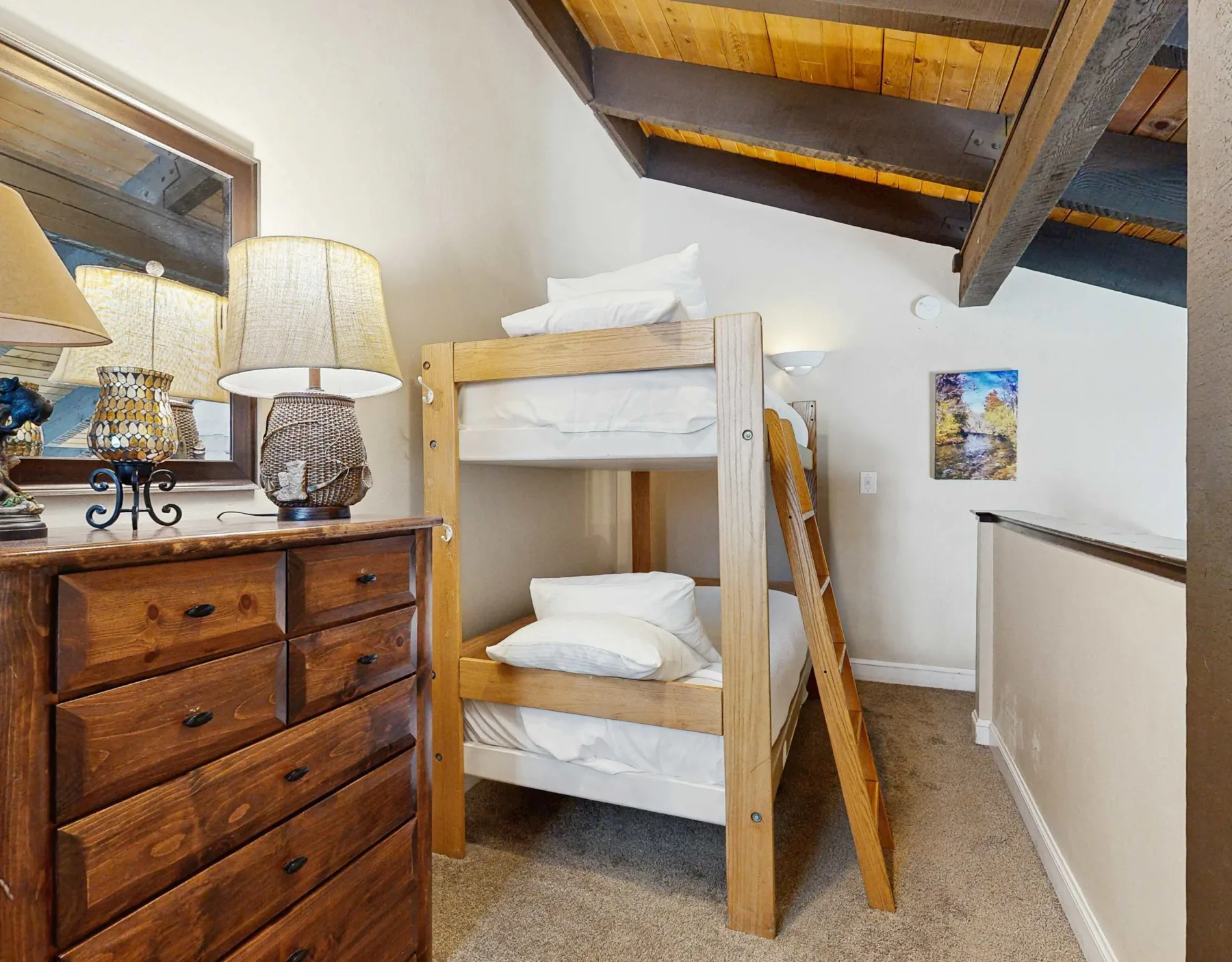 Un dormitorio con una litera de madera bajo un techo con vigas expuestas.