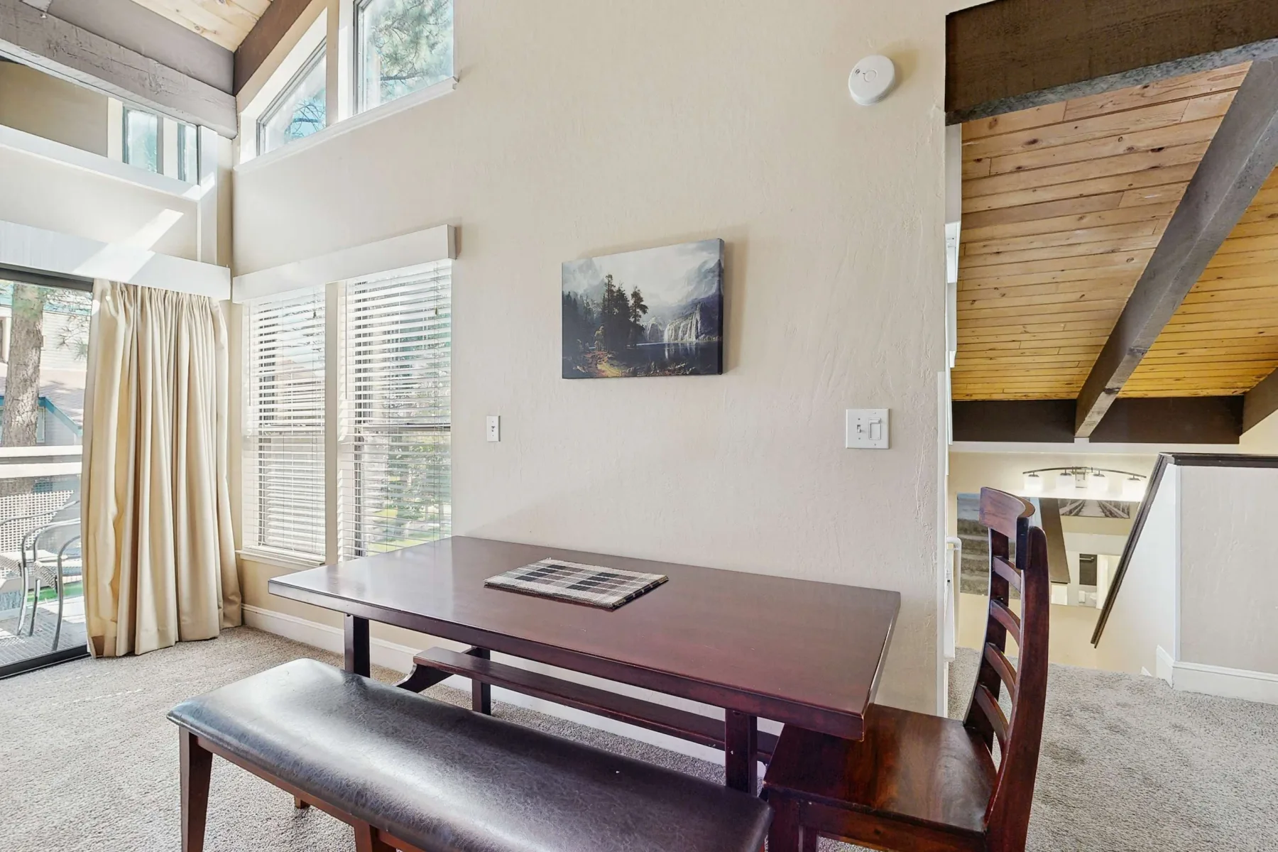Un comedor con una mesa larga y un banco junto a ventanas altas.