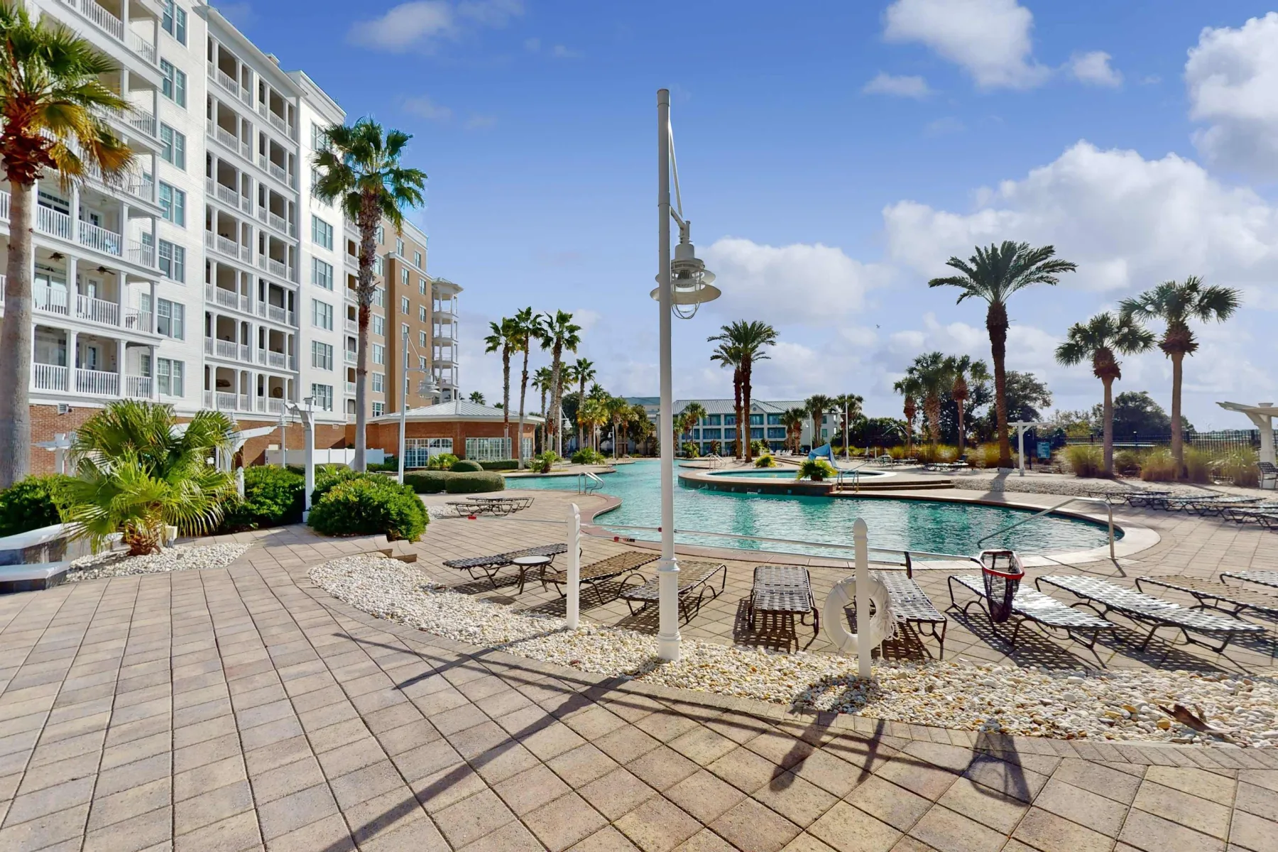 Shared amenity: Outdoor pool area beside a multi-story building, with palm trees and deck seating.