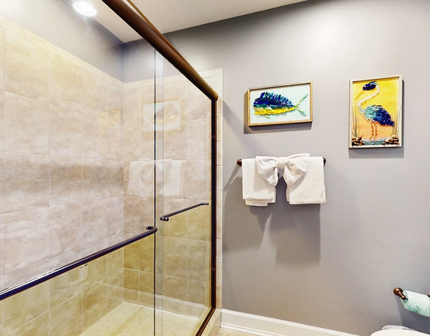 A tiled bathroom shower with a towel rack and framed artwork on the wall.