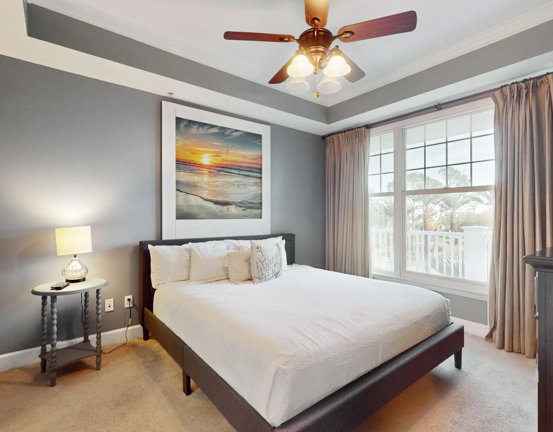 A bedroom with a neatly made bed beneath a framed seaside picture.