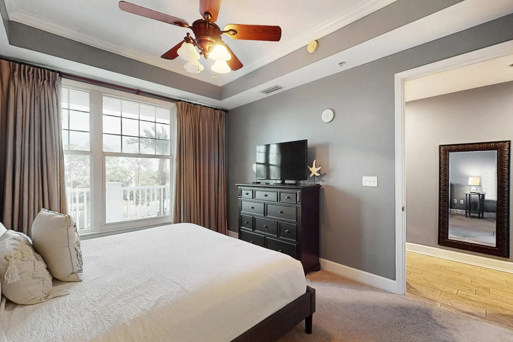 A bedroom with a bed beside a large window and a television on a dresser.