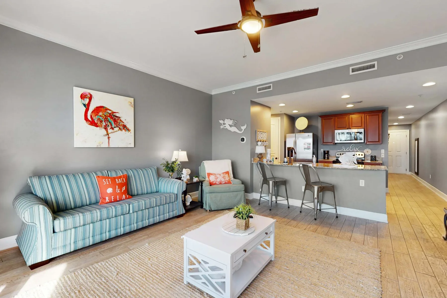 A living room opens onto a kitchen, with striped seating and a white coffee table.