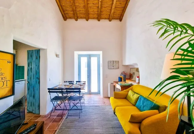 A bright living area with yellow seating, a dining table, and a television.