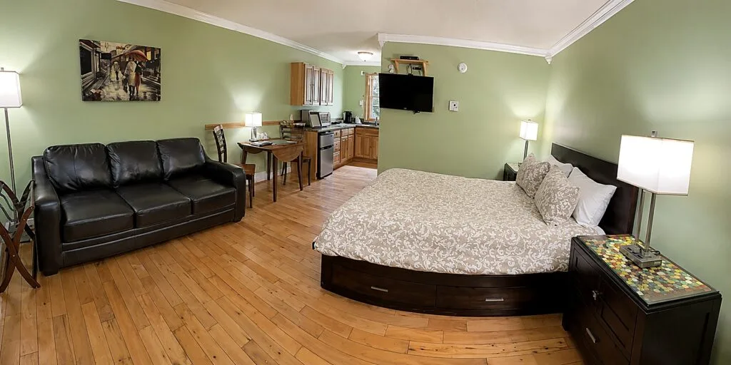 Representative hotel space: A bedroom with a large bed, a black sofa, and a small kitchen area.