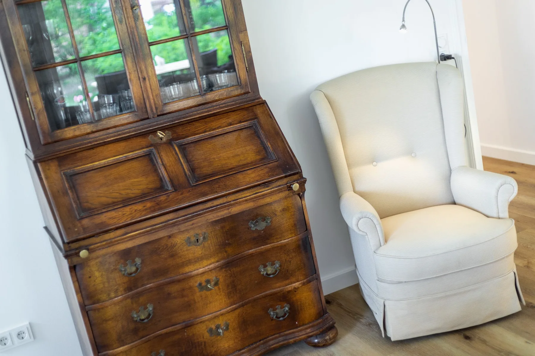 A bright room with a wooden writing desk beside a white upholstered chair.