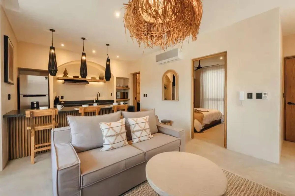 A bright open-plan living and kitchen area features a gray sofa, oval coffee table, and wooden dining counter.