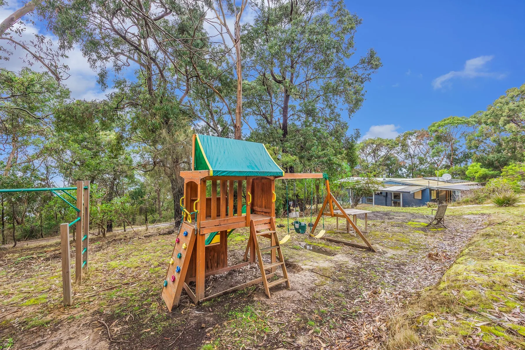 An outdoor wooden play structure with a slide and swings stands among trees.