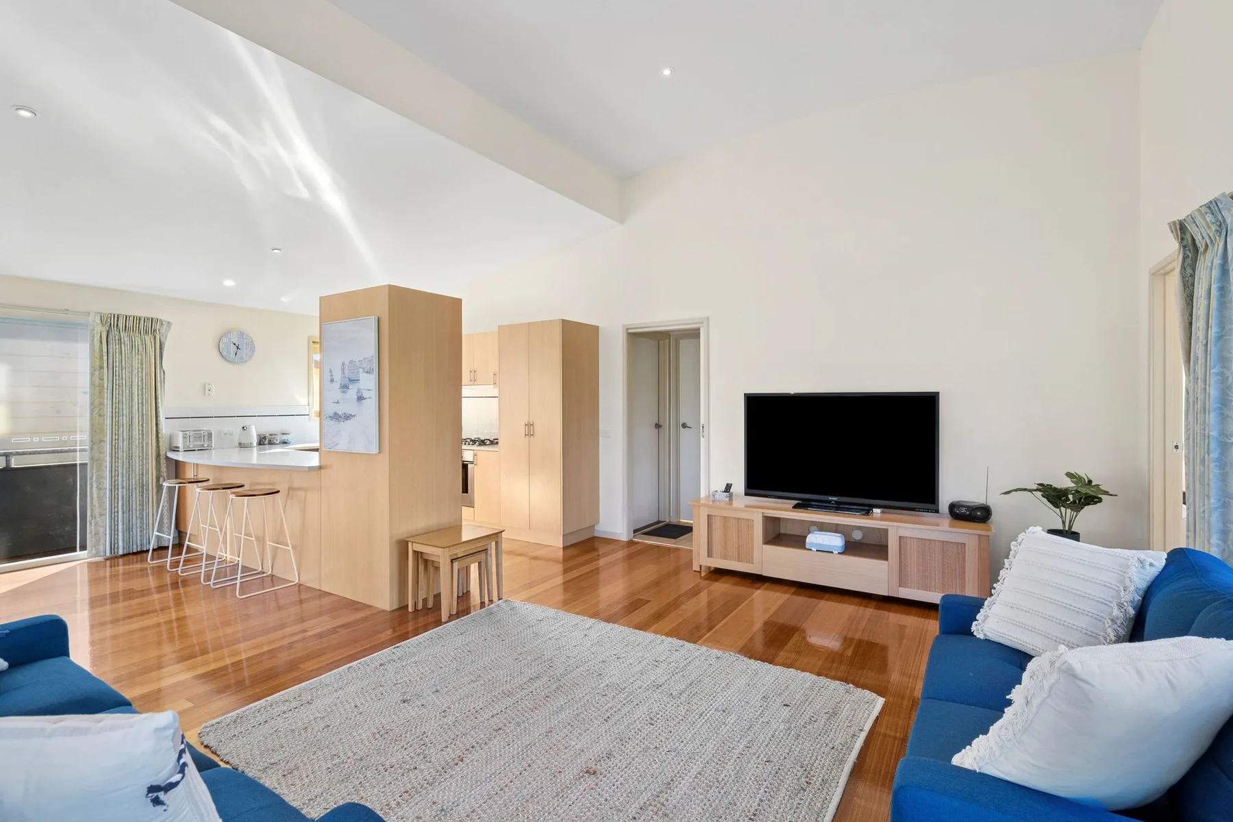 A bright open-plan living room with a kitchen area and blue seating.