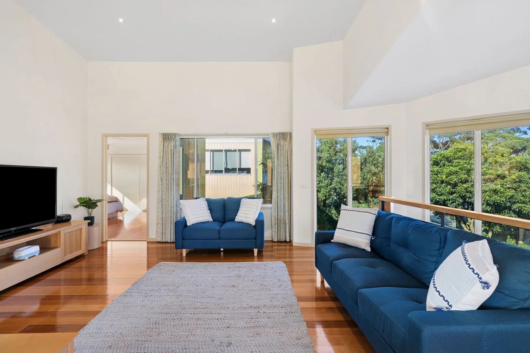A bright living room with blue seating, a television, and large windows.