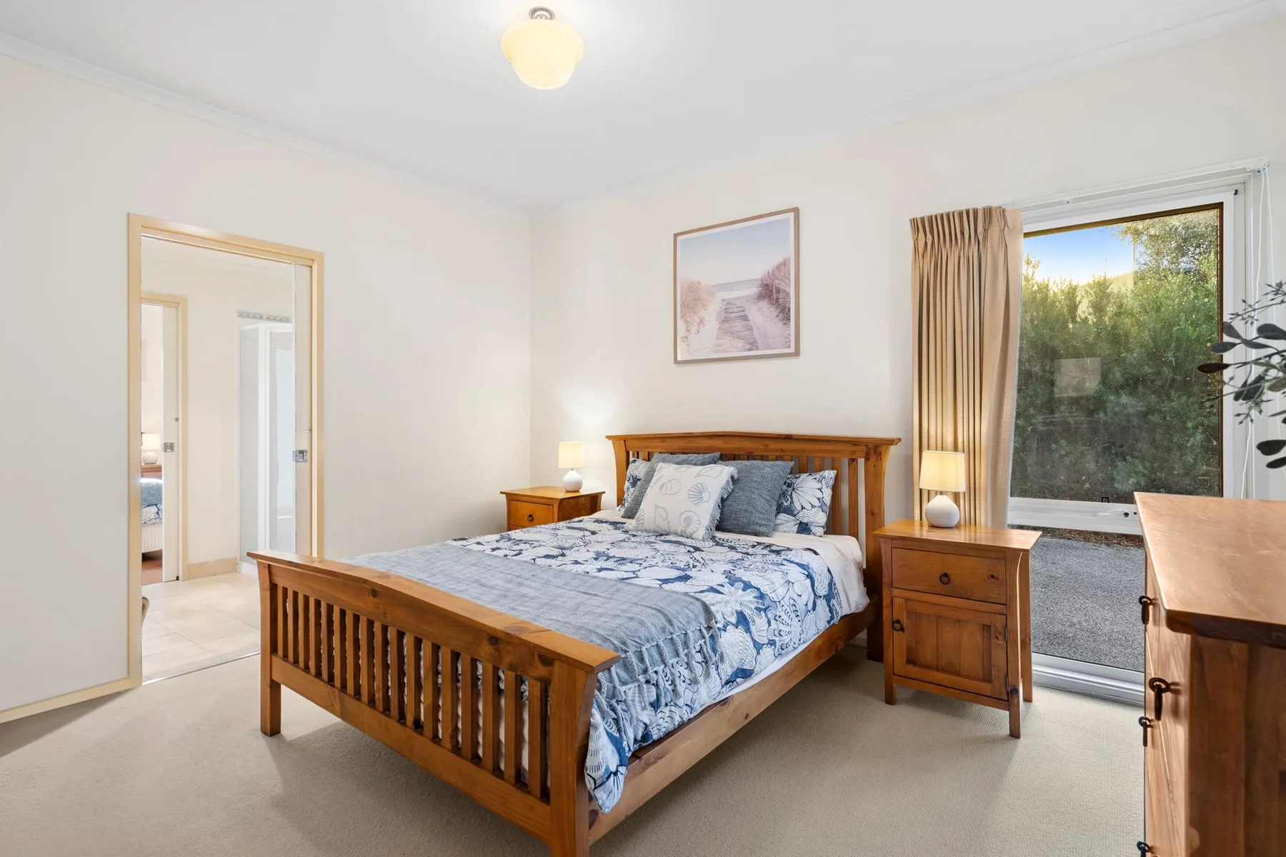 A bedroom with a wooden bed, blue bedding, and a window overlooking greenery.